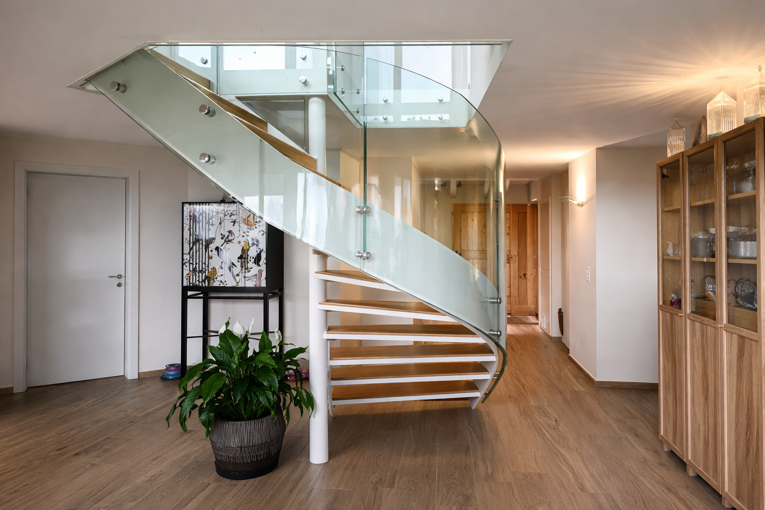 Escalier moderne en bois avec garde-corps en verre courbé sur mesure, installation intérieure design et lumineuse.